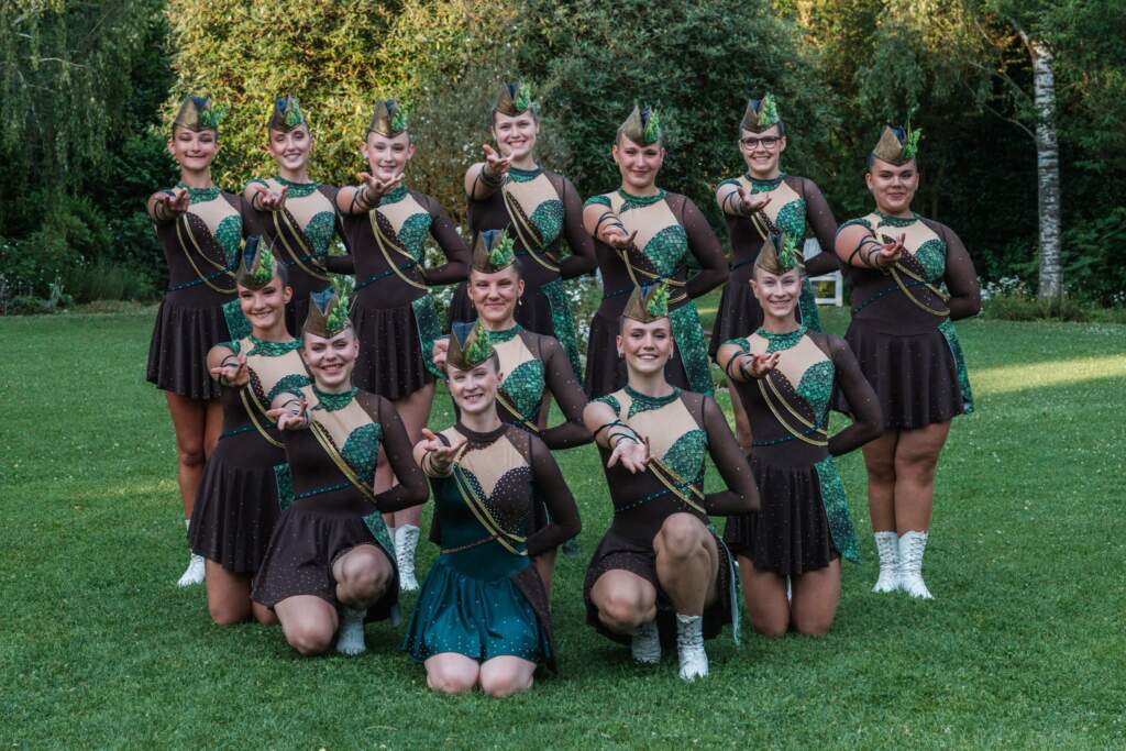 Seniorky v tmavě hnědých kostýmech se zelenými flitry a čepičkami s pérem